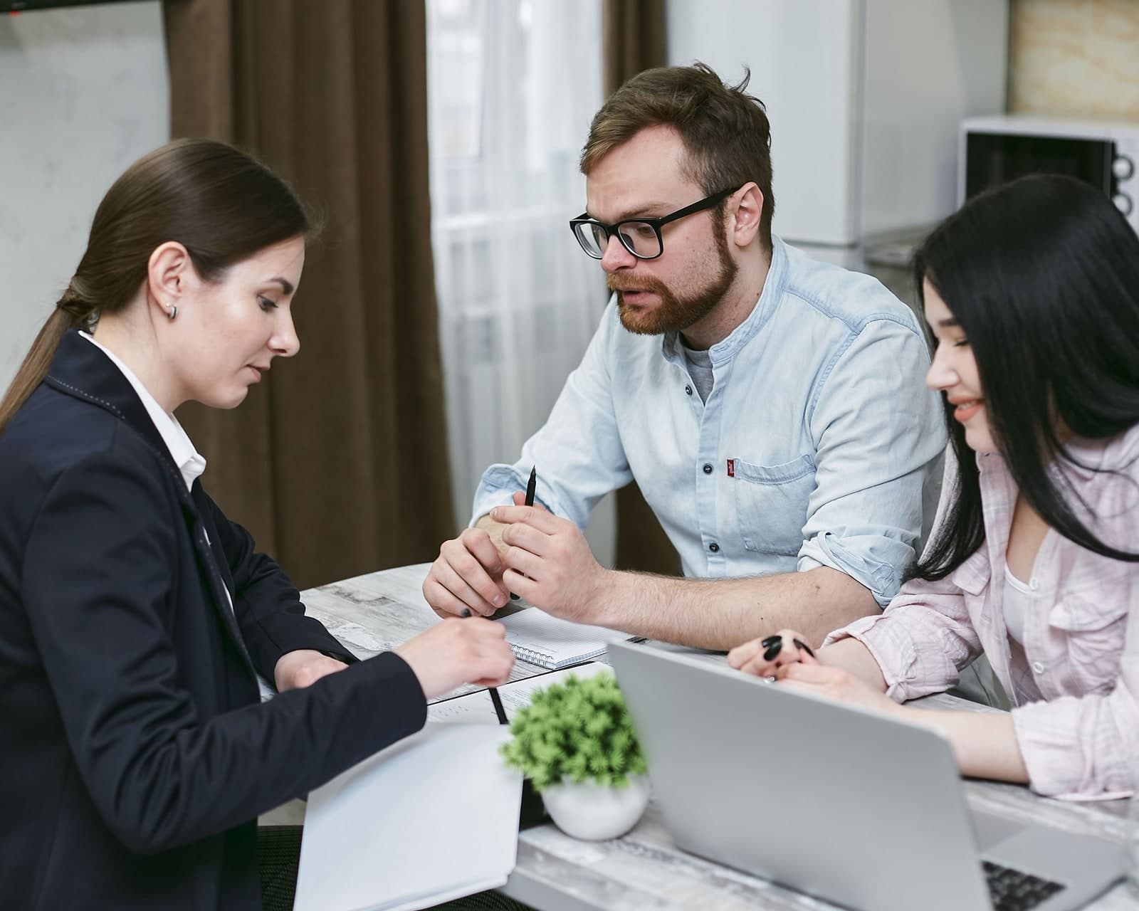 A financial adviser discussing paperwork with two clients across a table.