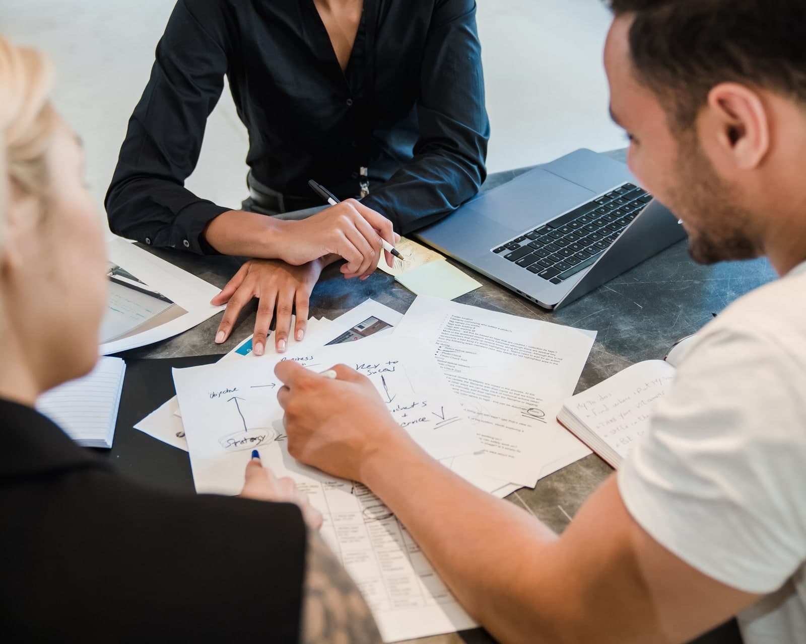 Three colleagues comparing documents and operating-model options around a table.