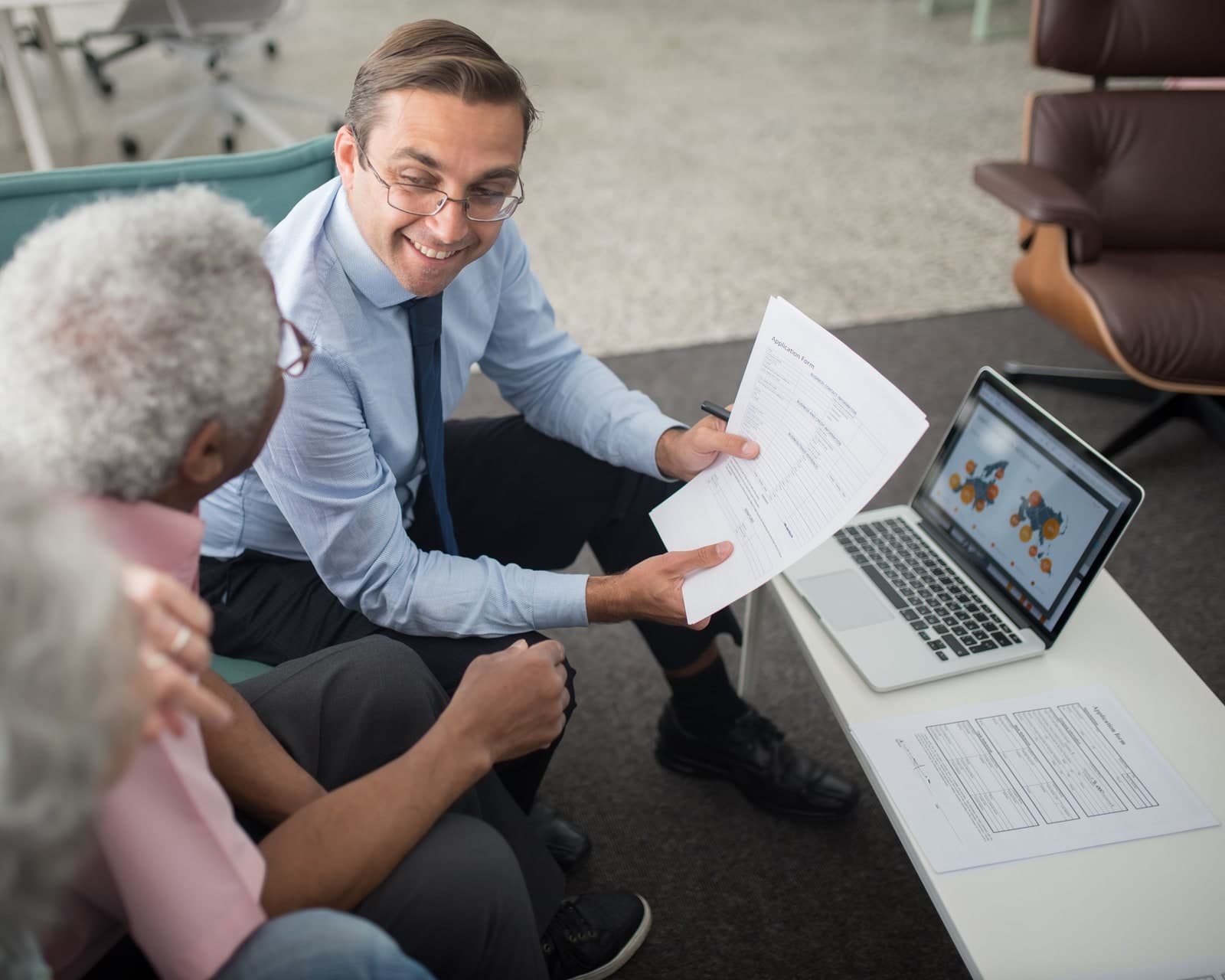 A financial adviser discussing pension documents with two older clients beside a laptop.